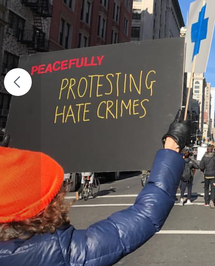 Janice, from behind, holding a protest sign that reads PEACEFULLY PROTESTING HATE CRIMES